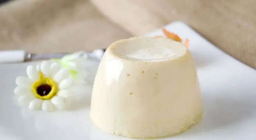 Delizioso budino fatto in casa, servito su un piatto bianco con un fiore decorativo.