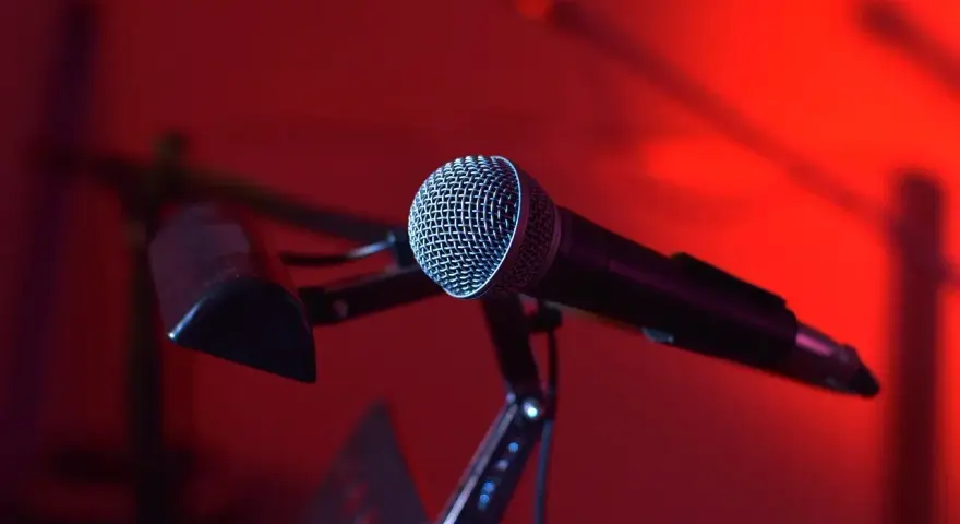 Mikrofon na statywie, gotowy do nagrania nastrojowego utworu w stylu trip hop. Czerwone światło tworzy atmosferę.