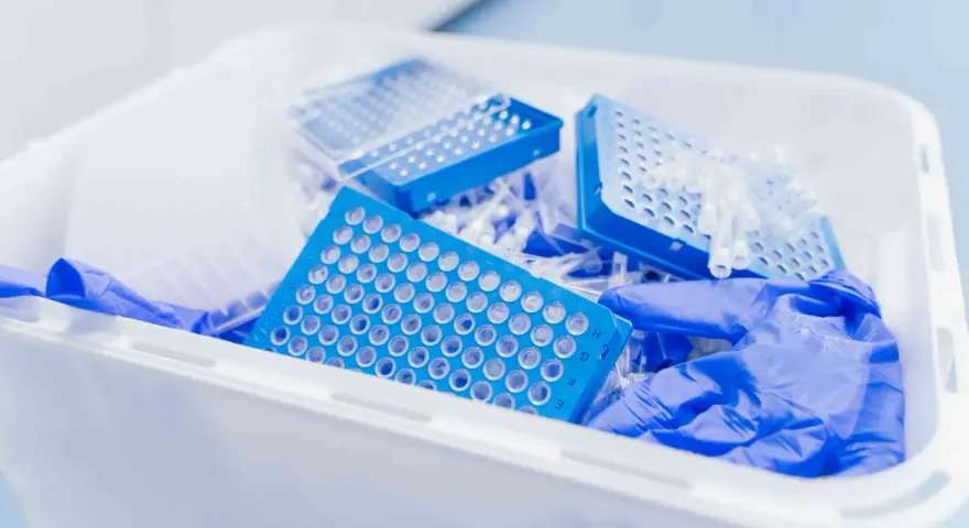 Niebieskie płytki do pipetowania i rękawiczki w pojemniku na odpady laboratoryjne. Kod odpadu 16 03 04.