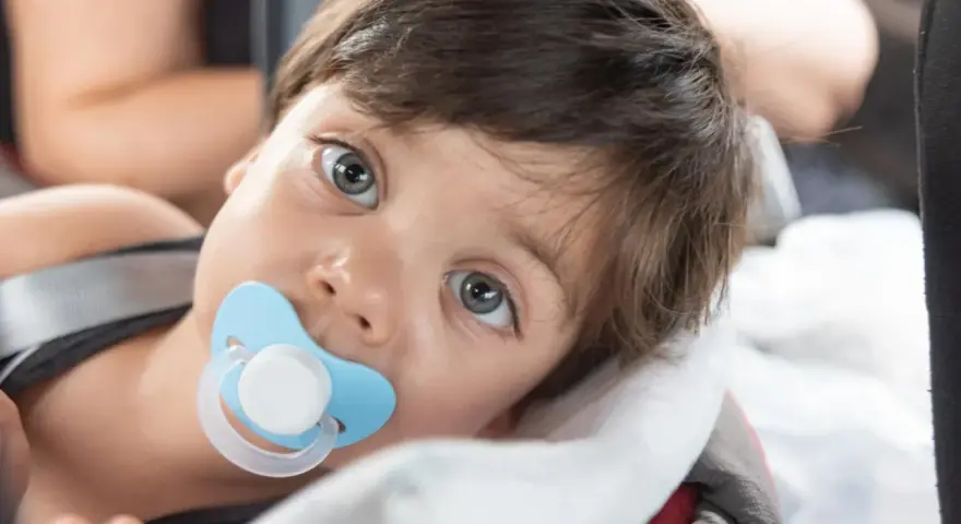 Małe dziecko z niebieskim smoczkiem Tommee Tippee w buzi, zapatrzone w dal.