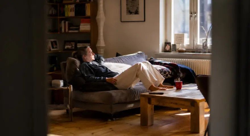 Frau liegt auf Sofa, genießt stille Meditation im warmen Sonnenlicht. Ein Moment der Ruhe im gemütlichen Wohnzimmer.