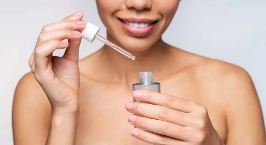 Une femme souriante applique un sérum. Elle se demande combien de temps entre sérum et crème pour une peau parfaite.