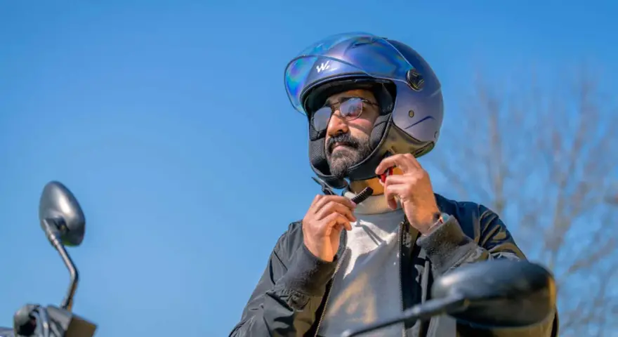 Uomo con barba che indossa un casco da moto blu iridescente, pronto per un giro.