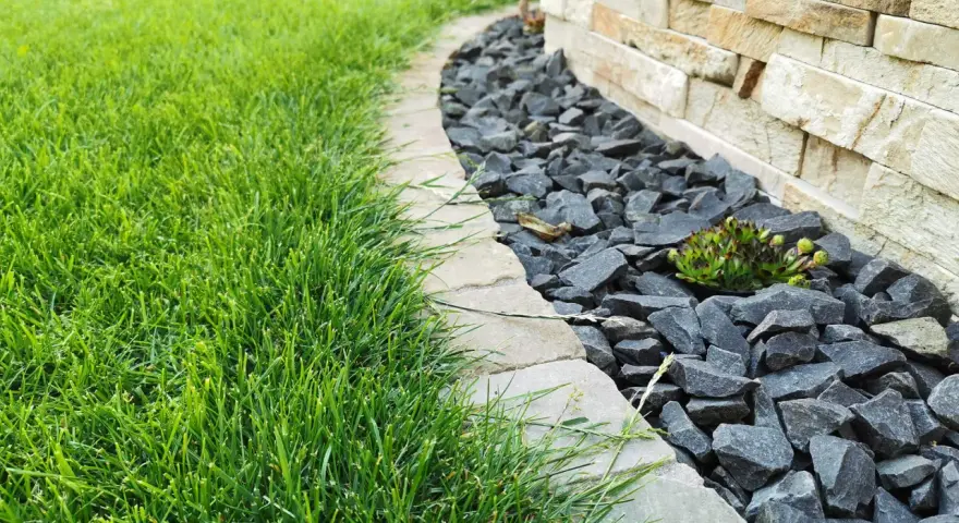 Ein Gartenweg mit frisch gemähten Rasen und grauen Bruchsteinen, die den Rand eines Beetes mit einer Sukkulente markieren. Die Pflastersteine schneiden eine klare Linie.