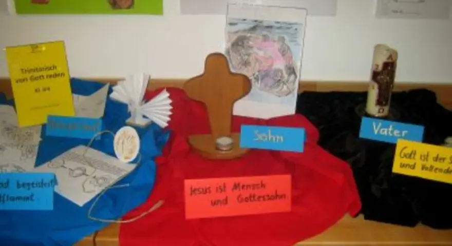Ein Kreuz, eine Kerze und Bilder zum Thema Trinität. Hier wird über den **Gottes Geist**, den Vater und den Sohn gesprochen.