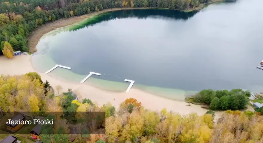 Jesioro Płotki jesienią. Piękna plaża, drewniane pomosty i kolorowe drzewa otaczają spokojną taflę wody.