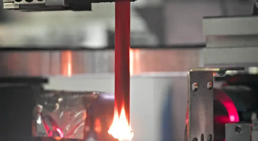 A red acrylic rod is tested for how acrylic fire resistant it is, with a flame licking its base.