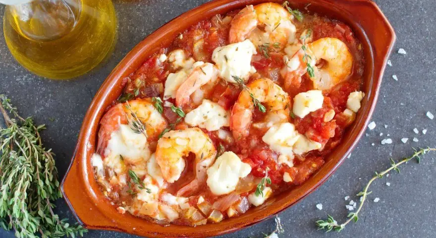 Gamberoni al guazzetto in terracotta, con pomodoro, formaggio fuso e timo. Un piatto invitante pronto per essere gustato.