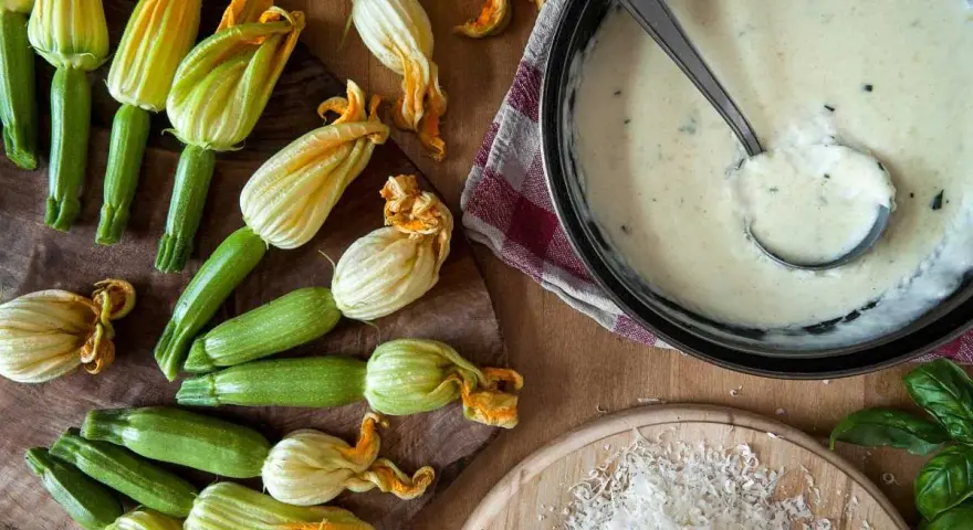Flores de calabacín frescas y una salsa cremosa en una sartén.