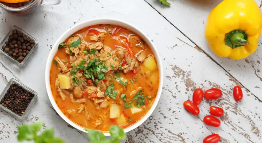 Gulasz warzywny z ziemniakami i papryką, idealny na dietę trzustkową. Obok kubek herbaty z pomarańczą i przyprawy.