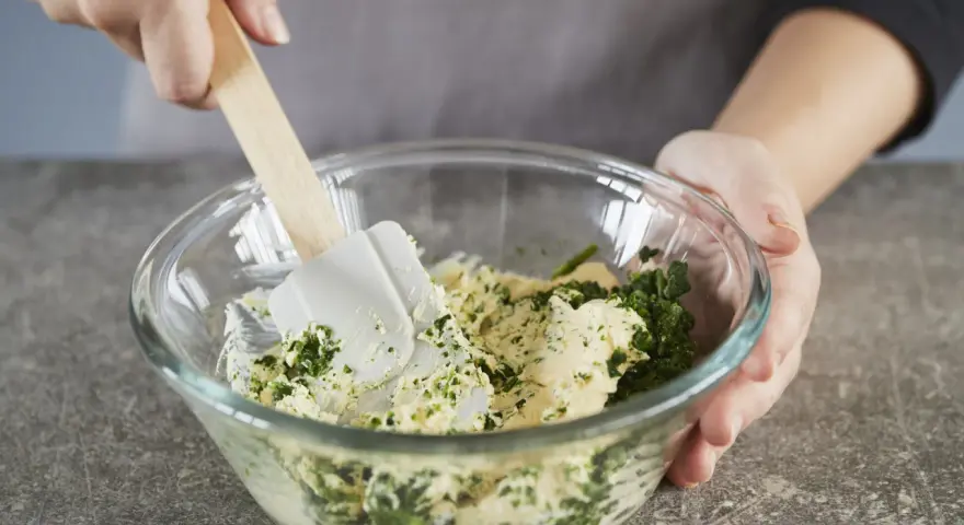 Hände mischen Kräuter und Butter in einer Schüssel. Perfekt, um Kräuterbutter selber zu machen.