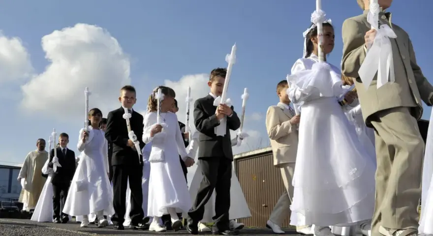 Kinder in festlicher Kleidung, was zieht man zur Kommunion an? Mädchen in weißen Kleidern, Jungen in Anzügen, alle tragen Kerzen.