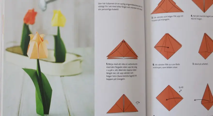 Vackra vika pappersblommor i form av tulpaner, en klassiker inom origamikonsten. En orange tulpan i förgrunden, med en röd och en gul i bakgrunden.