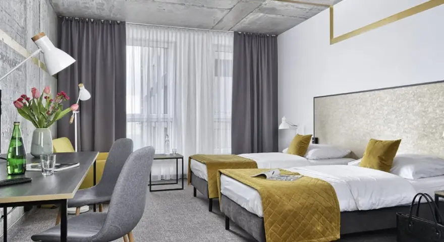 Pokój hotelowy z dwoma łóżkami, biurkiem i kwiatami. Idealne miejsce na wcześniejsze zameldowanie w hotelu.