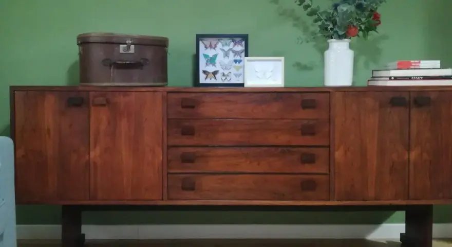 Mobile legno scolorito con cassetti e ante, decorato con una valigia vintage, cornici con farfalle e un vaso di fiori.