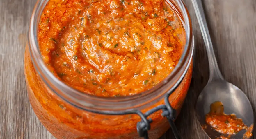 Vaso di pesto alla trapanese, un condimento rosso vivo con pomodori, mandorle e basilico, pronto per essere gustato.
