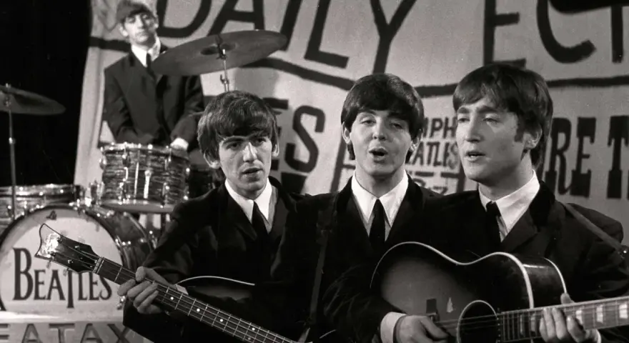 Les Beatles, le groupe le plus connu au monde, jouent sur scène. John Lennon et Paul McCartney chantent, George Harrison joue de la basse, Ringo Starr est à la batterie.
