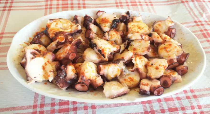 Pulpo a la gallega servido en plato blanco sobre mantel a cuadros rojos y blancos.