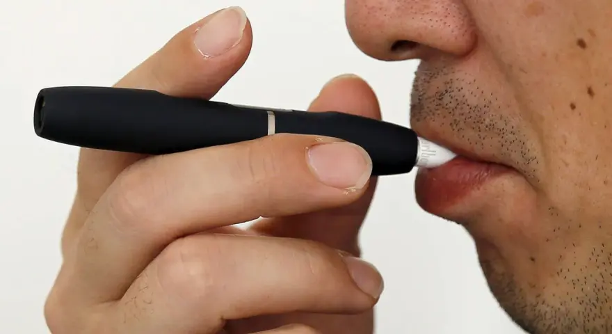 Persona usa un dispositivo IQOS. Las opiniones médicas sobre IQOS son variadas, pero este dispositivo calienta tabaco en lugar de quemarlo.