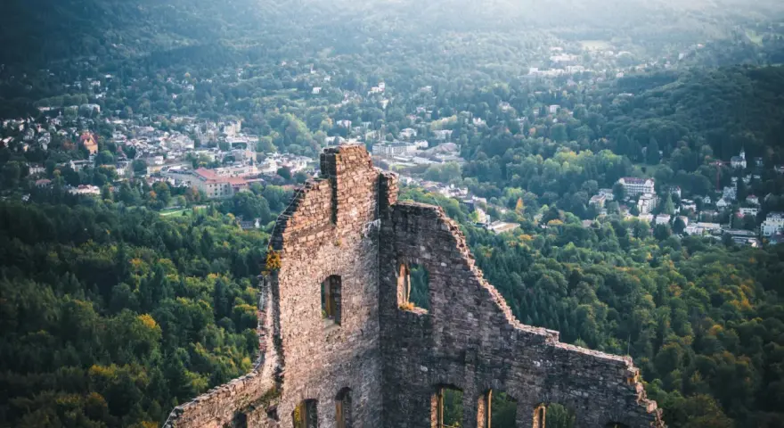 Ruinen einer Burg mit Blick auf eine Stadt und bewaldete Hügel.