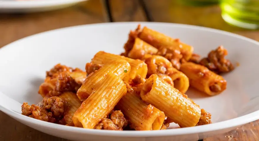 Rigatoni conditi con un ricco ragù di salsiccia, serviti su un piatto bianco.