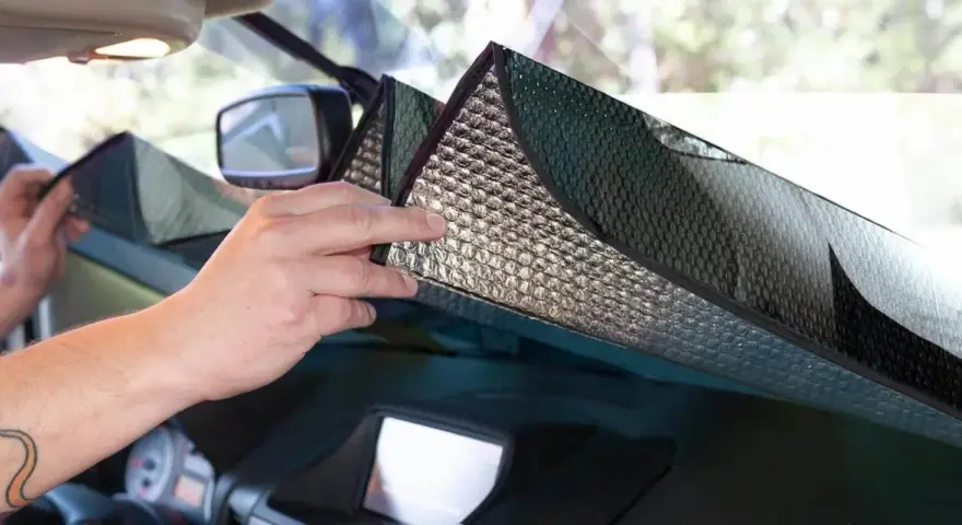 Mani che posizionano un parasole riflettente sul cruscotto per proteggere l'auto dal sole.