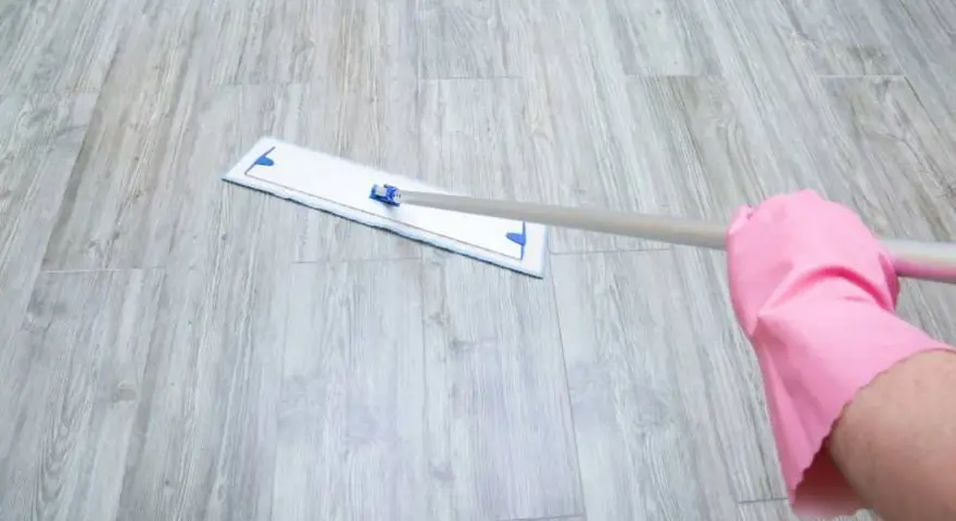 Mano con guante rosa limpiando suelo vinílico con mopa.