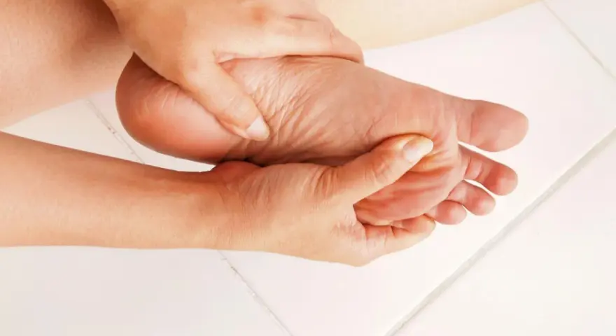 Dłoń masuje bolesną stopę, łagodząc objawy entezopatii rozcięgna podeszwowego.