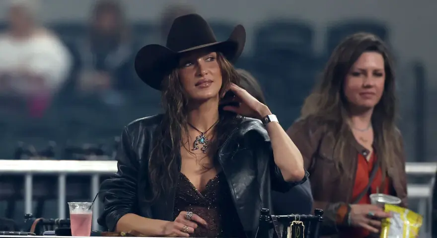 Mujer con sombrero tejano y chaqueta de cuero, disfrutando de un evento. Se aprecian otros tipos de tejanos en el público.