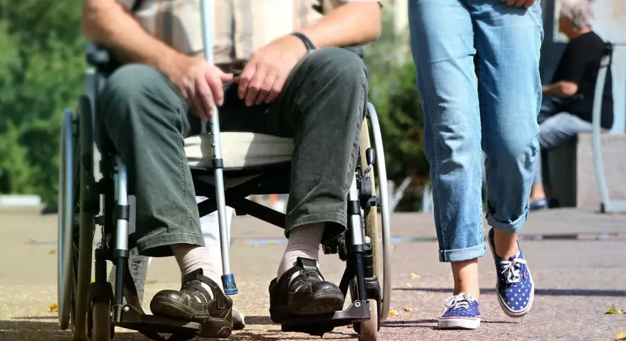 Osoba na wózku inwalidzkim z laską obok idącej osoby. Ulga na śmieci dla niepełnosprawnych to ważny temat.