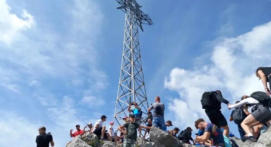 Tłum ludzi na skalistym szczycie podziwia imponującą wysokość krzyża na Giewoncie.
