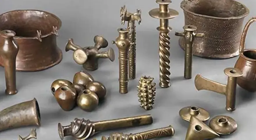 Colección de **herramientas de la edad de los metales**, incluyendo vasijas, soportes y objetos ornamentales de bronce y cobre.