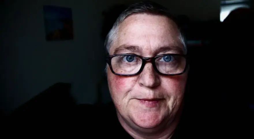 Mężczyzna z niebieskimi oczami i okularami. Jego **czerwona twarz** emanuje ciepłem, a na policzkach widać rumieńce.