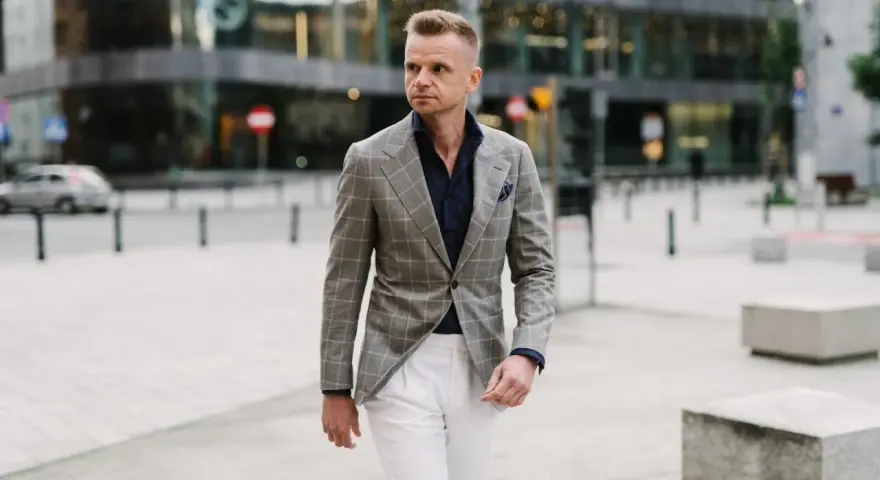 Elegancki mężczyzna w szarej marynarce w kratę i białych spodniach. Idealne połączenie, jeśli zastanawiasz się, jakie spodnie do szarej marynarki pasują.