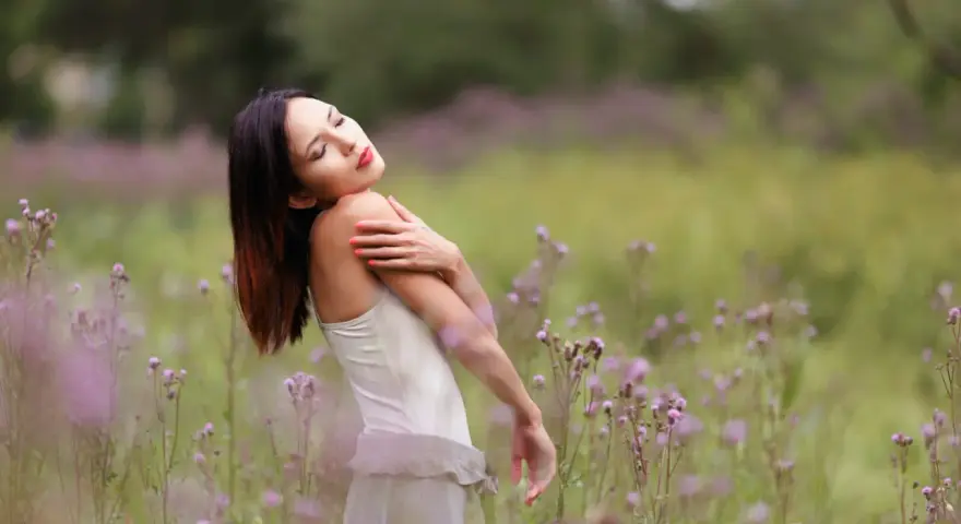 Portrait en bokeh d'une femme aux yeux fermés, bras croisés sur la poitrine, dans un champ de fleurs sauvages mauves.