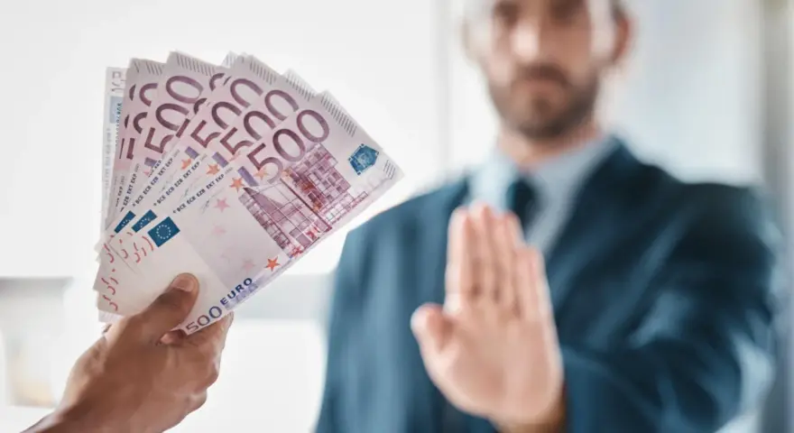 Ręka podaje plik banknotów 500 euro. Mężczyzna w garniturze odrzuca ofertę, mówiąc, że klient nie zapłacił za usługę.