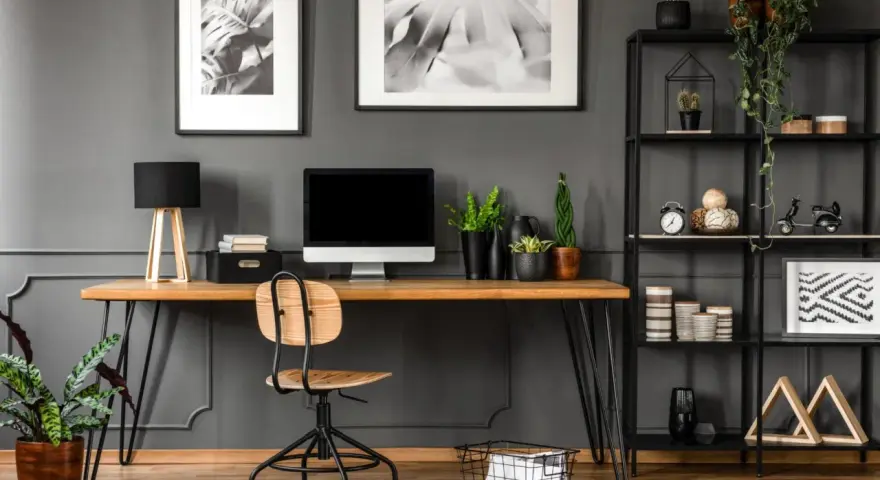 Arredamento studio casa: scrivania in legno con computer, sedia, piante e libreria nera piena di oggetti decorativi.