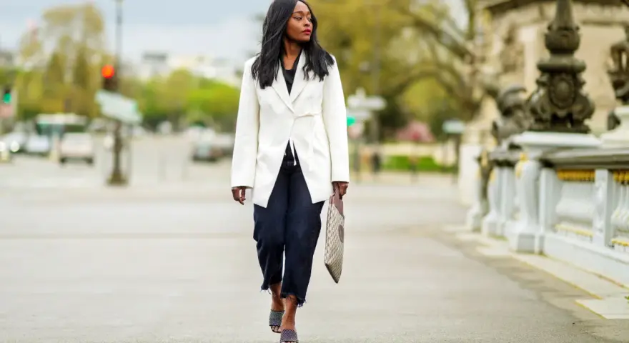 Mujer con un look smart elegant, lleva un blazer blanco, jeans oscuros y sandalias de diseño.