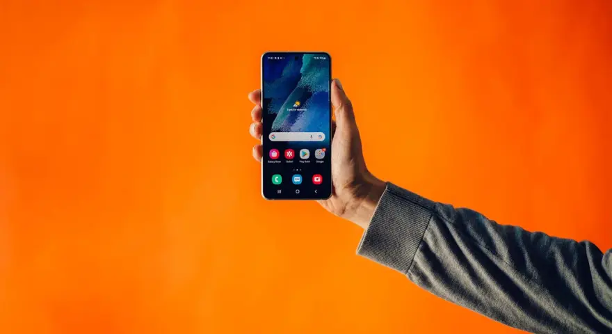 En hand håller upp en Samsung-telefon med dubbla SIM-kort mot en orange bakgrund.