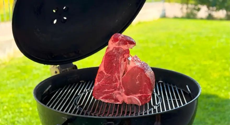 Una succulenta bistecca fiorentina cruda riposa sulla griglia di un barbecue, pronta per essere cucinata all'aperto.