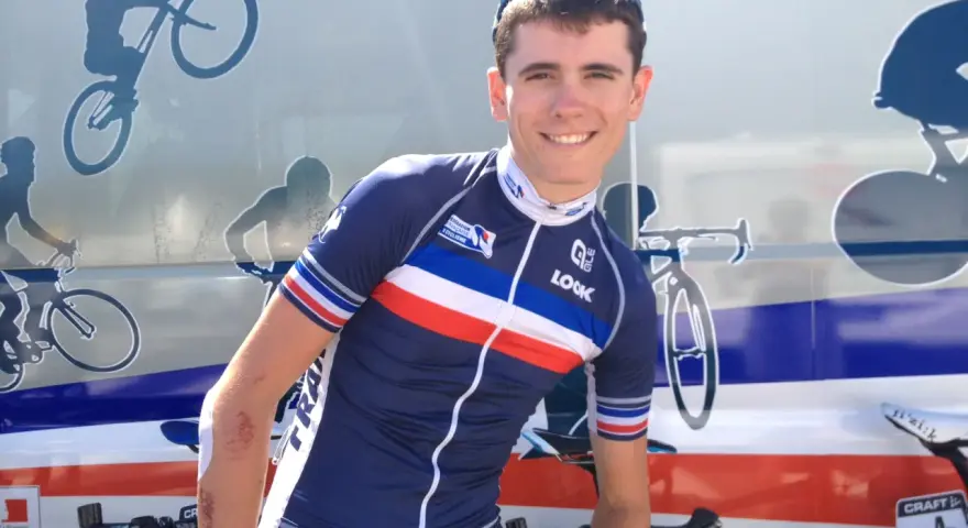 David Gaudu, a French cyclist, smiles in his team's blue, white, and red jersey, with bike graphics on the vehicle behind him.