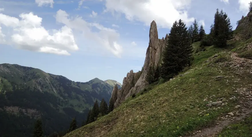 Ein steiler Bergpfad führt am markanten Siplinger Kopf vorbei, umgeben von grünen Hängen und Nadelbäumen.