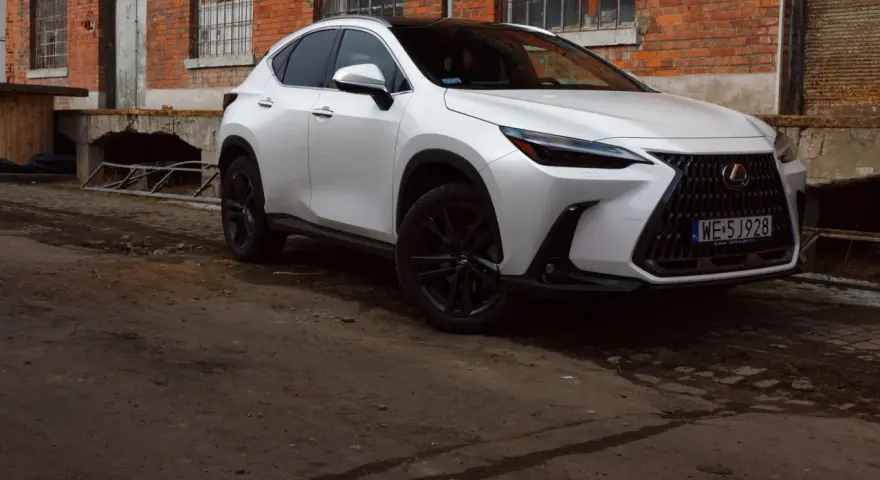 Biały Lexus 350h z czarnymi felgami stoi przed starą ceglaną budowką.