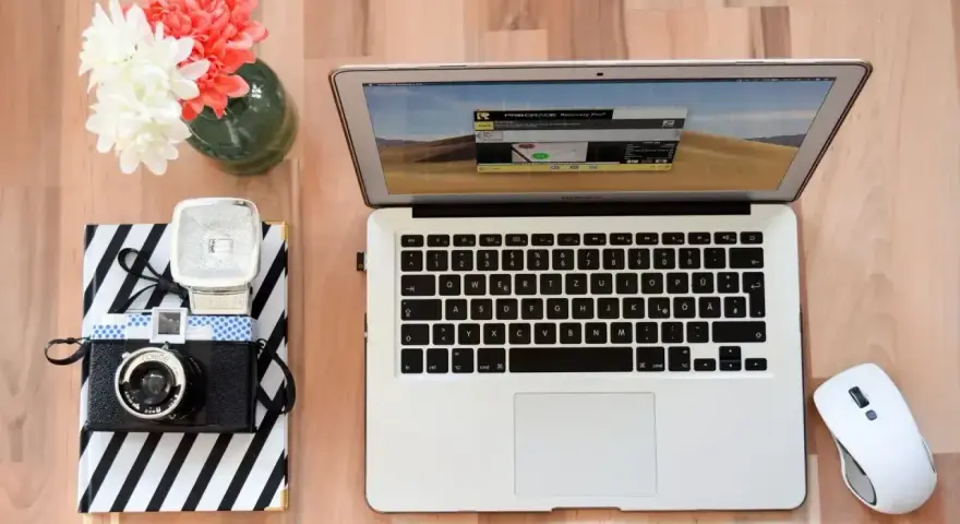 Jak zgrać zdjęcia z aparatu na laptop? Na biurku leży aparat, laptop i myszka.