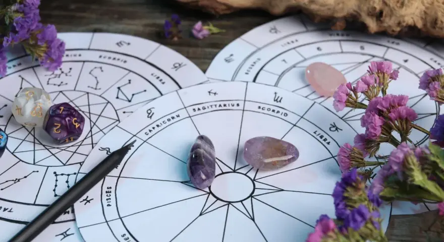 Astrologiczne koła zodiaku, kamienie, kostki i fioletowe kwiaty. 27 wrzesień znak zodiaku to Waga, symbolizująca równowagę.