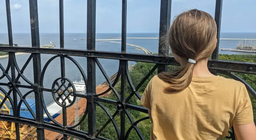 Dziewczynka podziwia widok z najwyższej latarni morskiej w Polsce. Widać morze, port i statki.