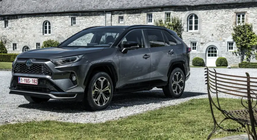 Szary Toyota RAV4 Hybrid przed kamiennym budynkiem. Zastanawiasz się, ile kosztuje Toyota RAV4 Hybrid?