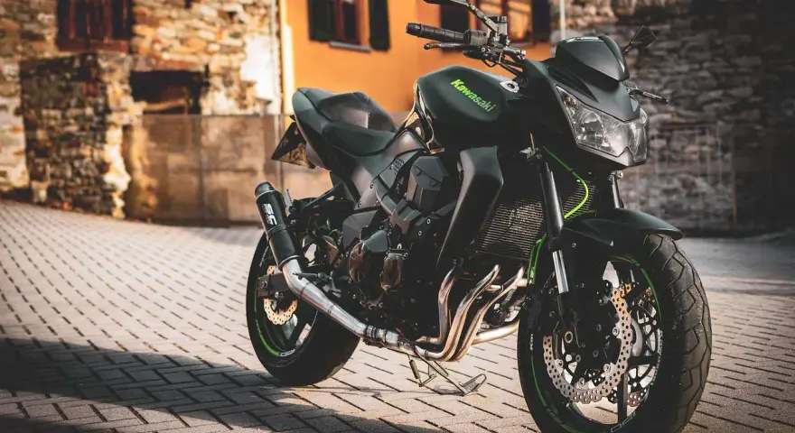 Czarny motocykl Kawasaki na brukowanej ulicy, z budynkami w tle.