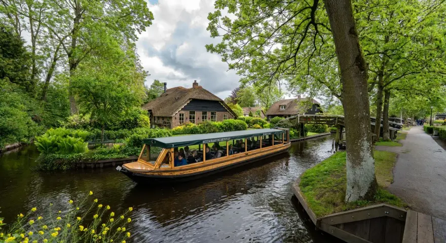 Bootfahrt durch Giethoorn, das Venedig der Niederlande. Grüne Ufer, Reetdachhäuser und gelbe Blumen am Wasser.