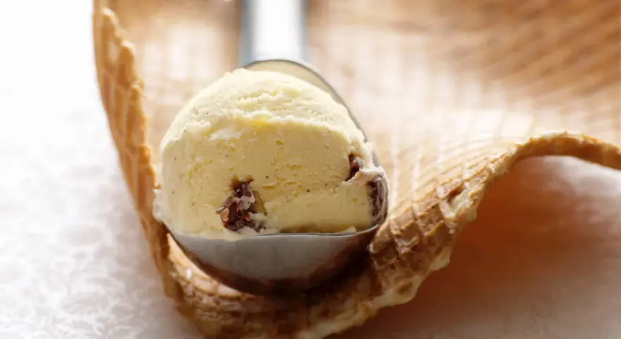 Ein Löffel cremiges Eis mit Rosinen und einem Hauch Rum ruht auf einem Waffelrand.
